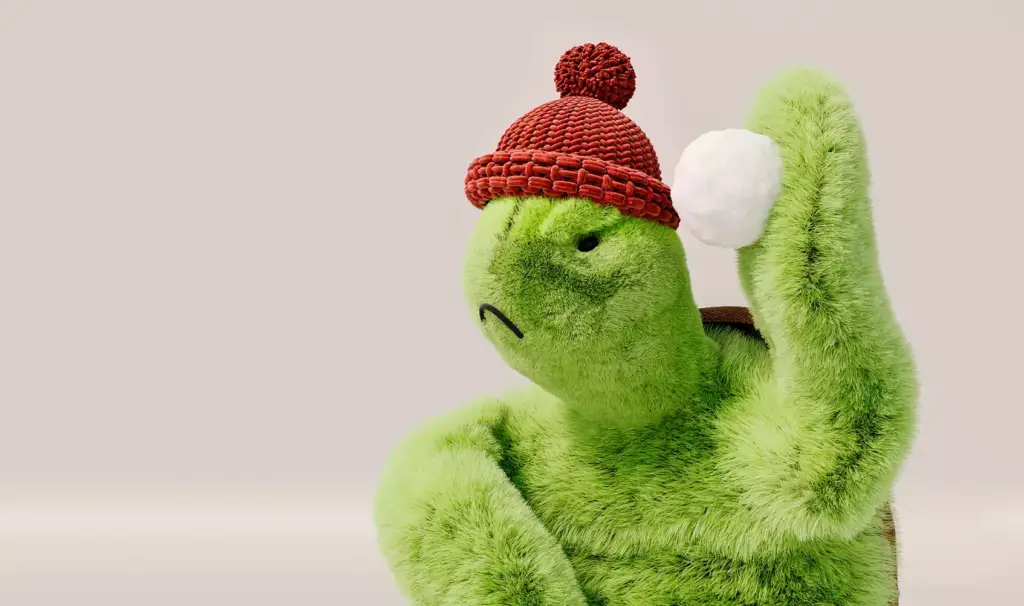 3D product render close up of green turtle plush wearing red knit hat holding white snowball