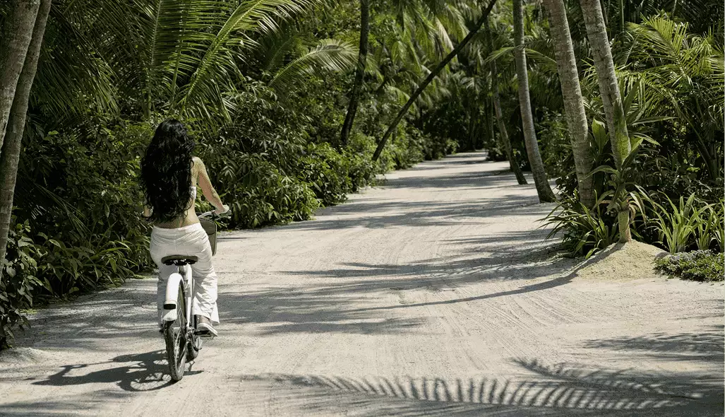 Cyclist in 3D hotel renderings rides a sandy path through dense palms and tropical greenery