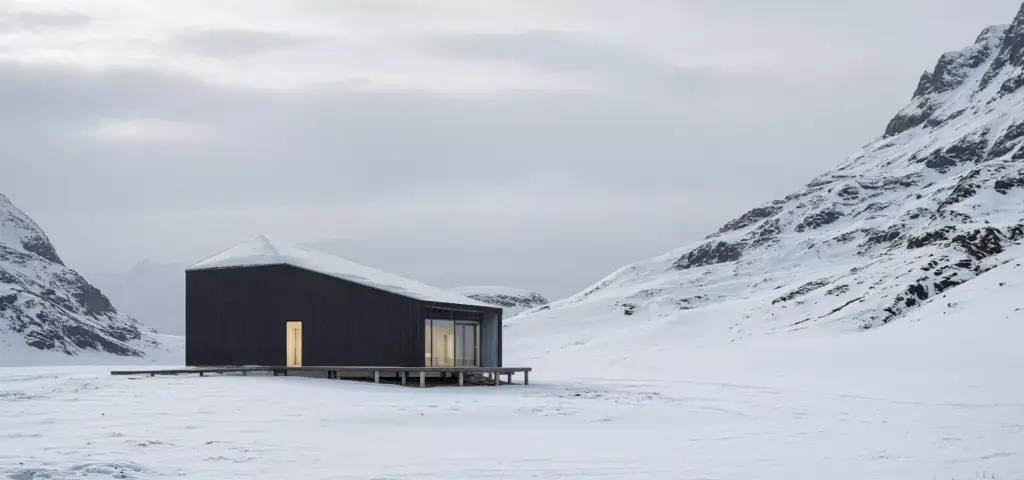 Winter rendering of a dark cabin in a snowy mountain valley with a lit doorway and overcast sky