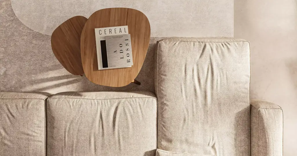 Beige sofa in apartment interior with small wooden tables and books on top