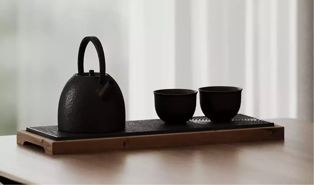 Tea set with kettle and cups on wooden tray near window light, black apartment design