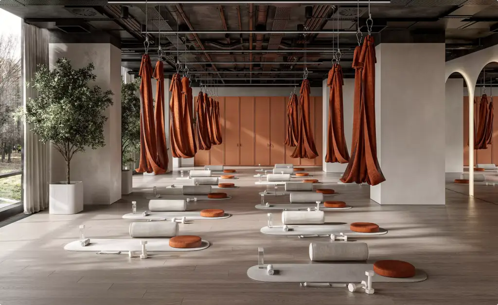 Aerial yoga studio fitness center interior design with suspended hammocks, mats, cushions, and large windows