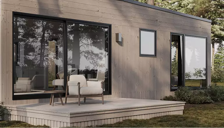 Modern forest house exterior with wood siding, patio chairs, and large glass doors in pine forest