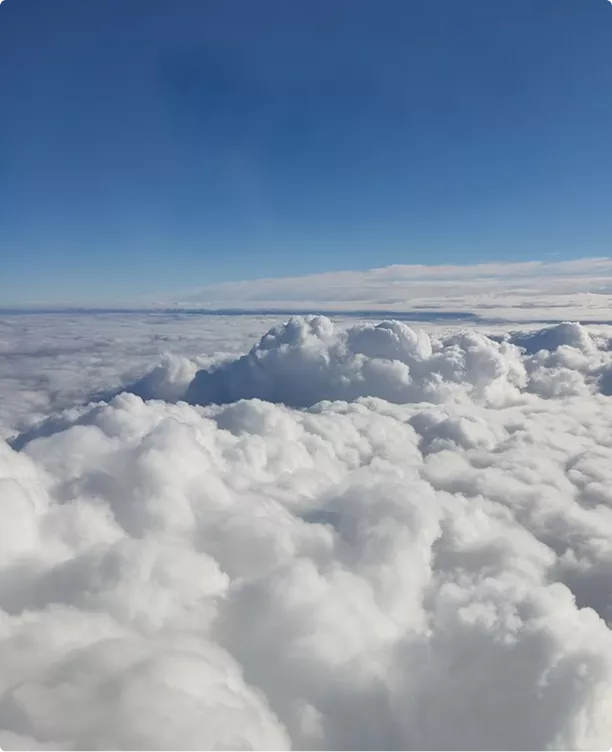 Cloud layer from above under blue sky showing soft cloud tops and horizon aircraft design context