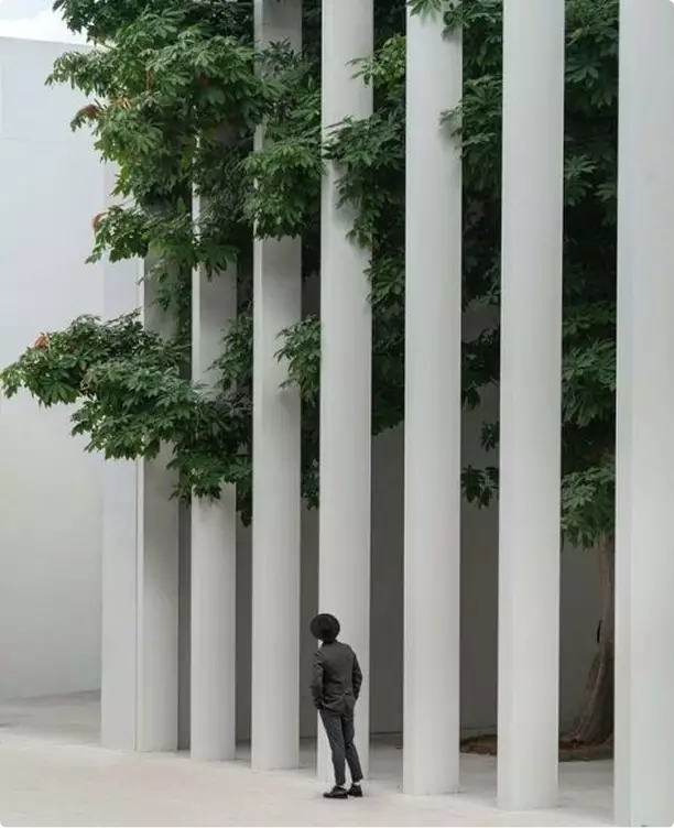 Industrial 3D rendering of vertical columns with trees and person walking in landscaped exterior space