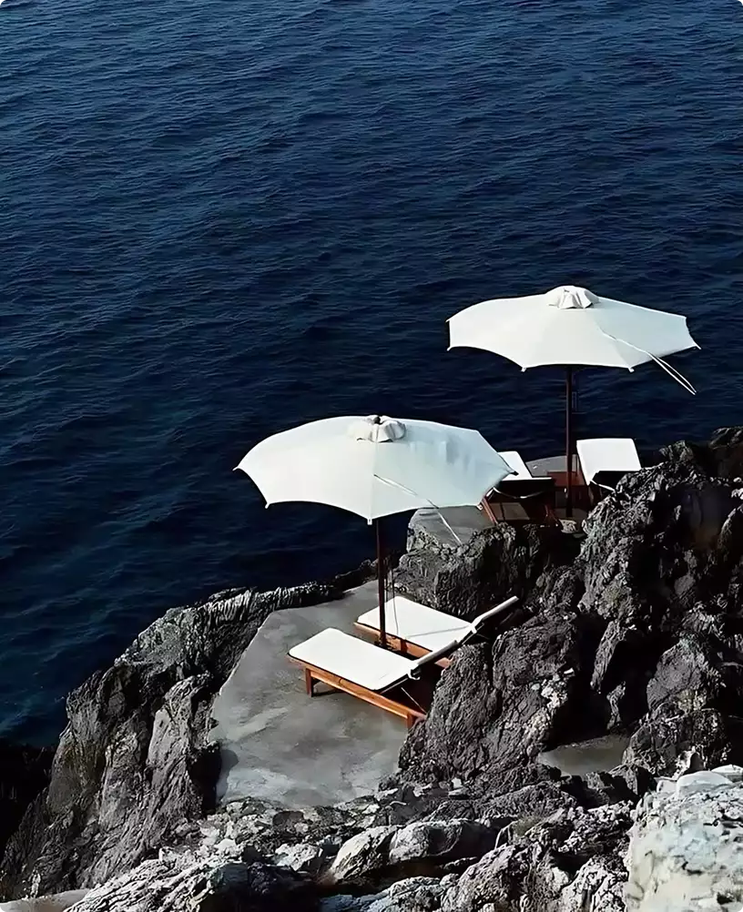 3D yacht visualization of white lounge chairs and umbrellas on rocky seaside cliffs