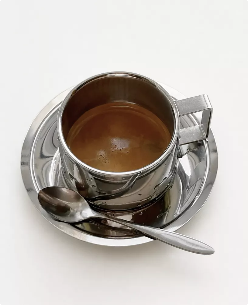 Metal coffee cup on saucer in cafe interior CGI with spoon on white background