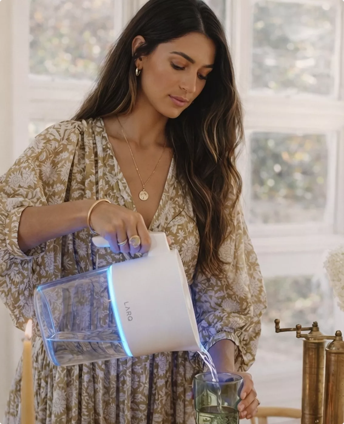 Woman pouring water from glowing white LARQ pitcher visualization into drinking glass