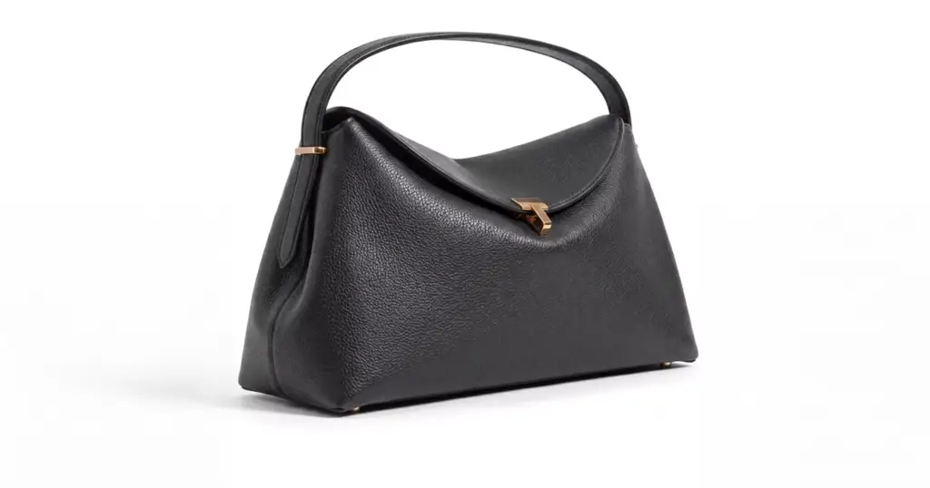 Black Toteme handbag with curved handle and gold clasp on gray background