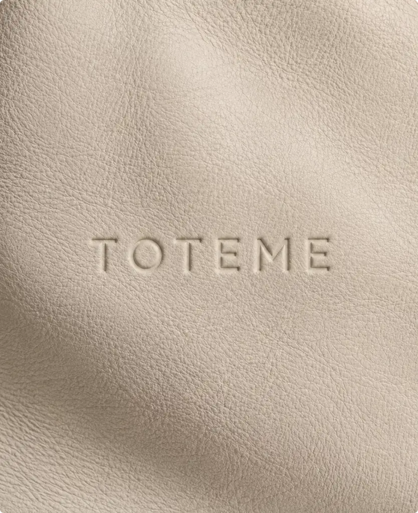 Embossed Toteme logo on beige textured leather surface