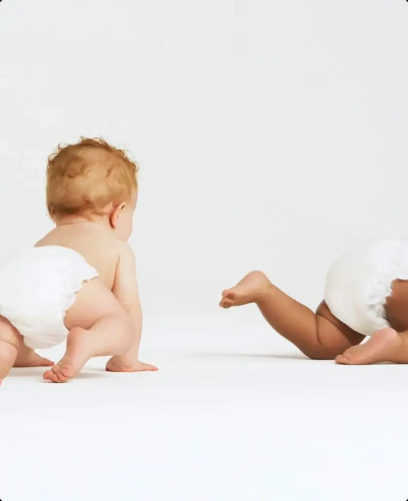 Two babies crawling in white diapers on a studio backdrop, baby diaper product visualization.