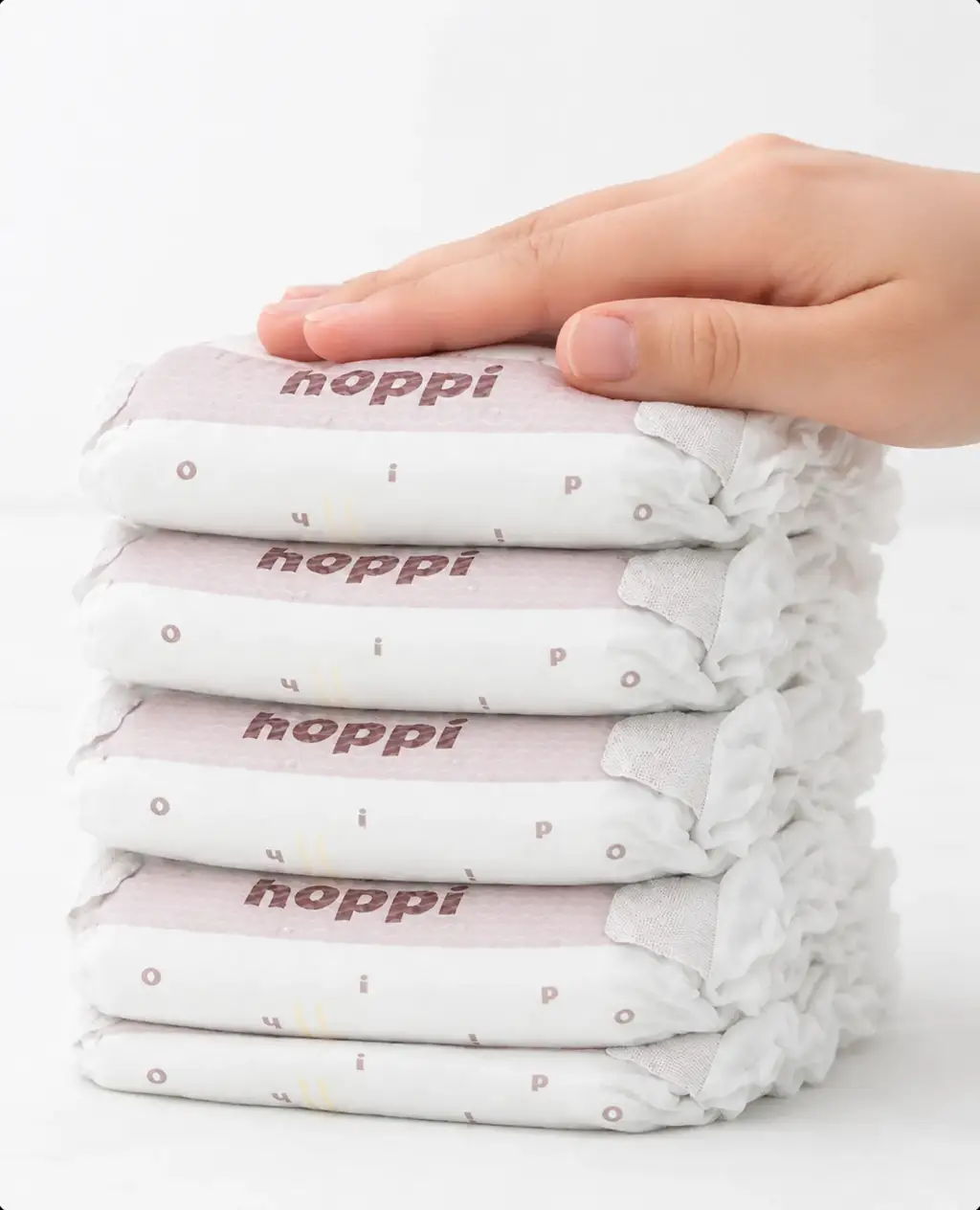 Hand resting on a neat stack of hoppi diapers, baby diaper marketing visual.