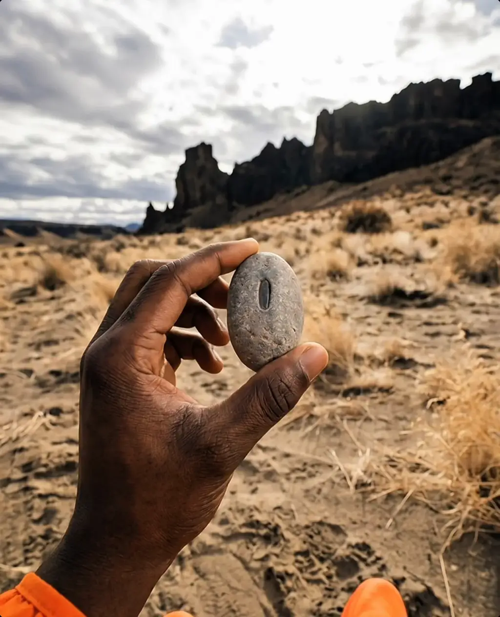 Hand holding an engraved stone in a desert landscape.