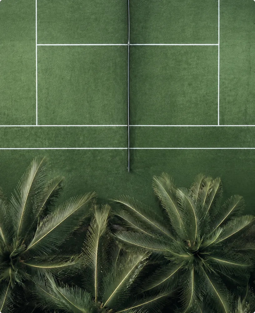 Detail of padel court equipment at the entrance, showing surface texture and glass-wall integration with the surrounding garden.