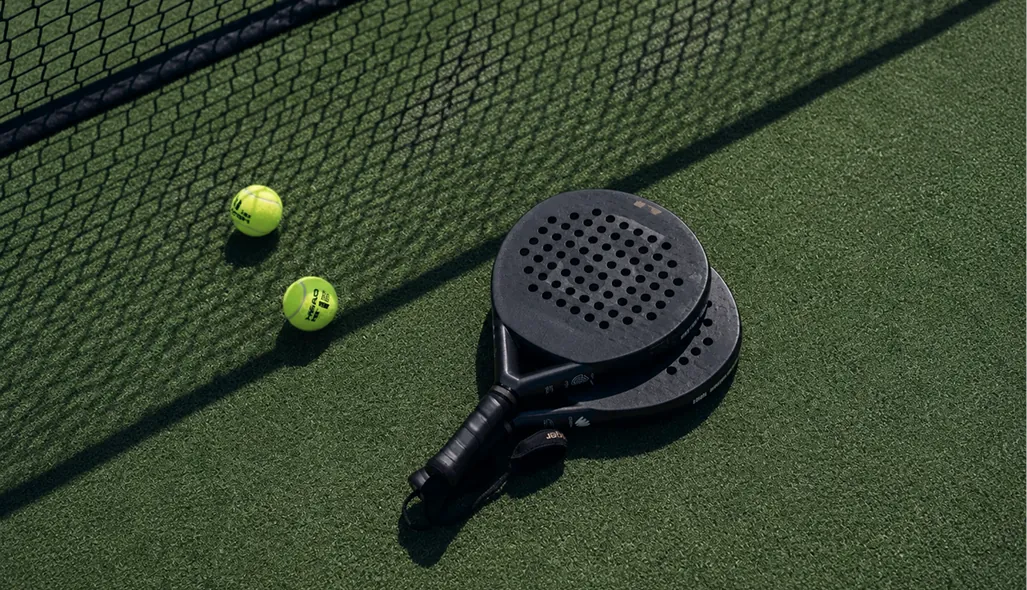 Close-up CGI render of a padel racket and ball detail, showing material accuracy and lighting on the court surface.