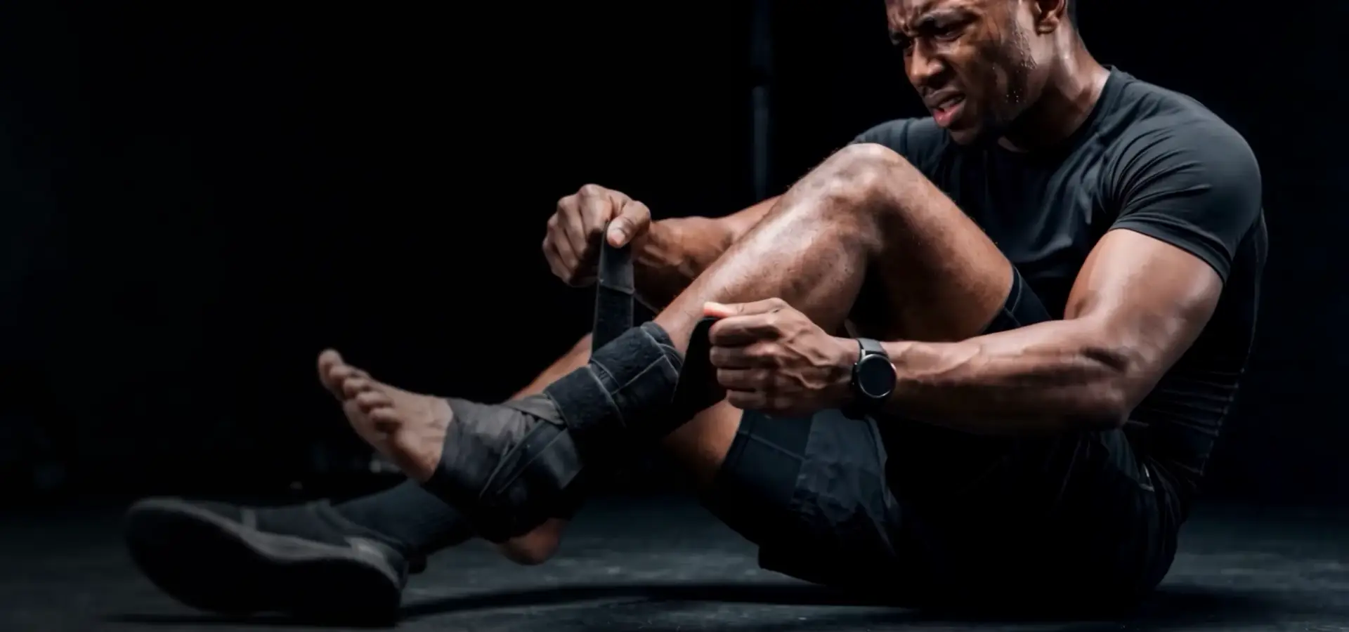 Athlete sitting in a dark studio wrapping an ankle support, sports equipment product visualization hero.