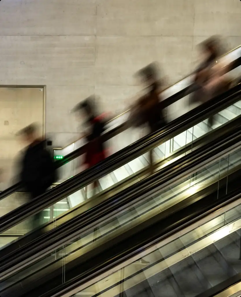 Commuters moving on an escalator in motion blur, illustrating the busy daily life a digital health app is built for.